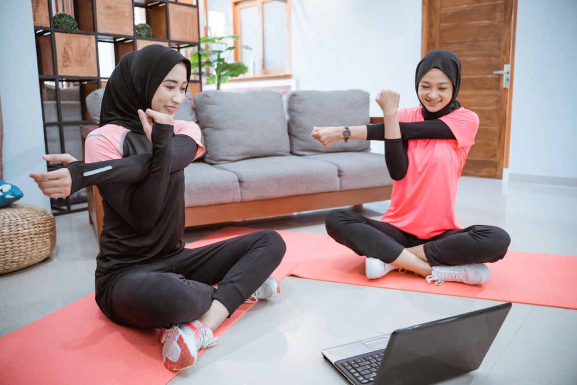 two-muslim-women-sports-clothes-sit-warming-up-stretching-their-arms-home (Medium)